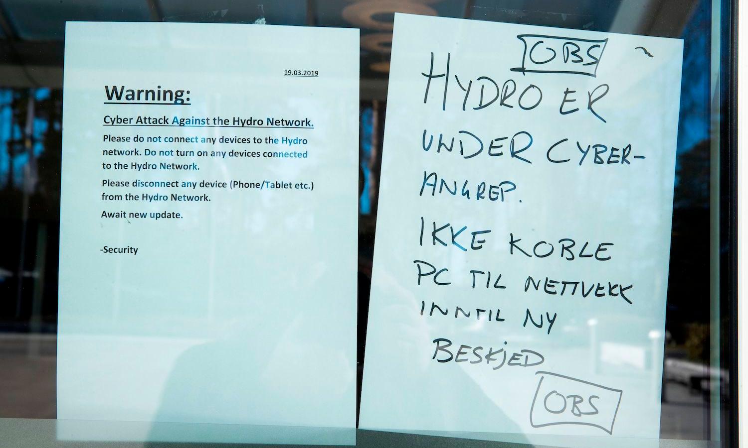 A sheet of paper with informations concerning a cyber attack (L) and one reading &#8216; Hydro is under a cyber attack, don&#8217; t plug your computer on the network unless we say so&#8217; are pictured on a window of the headquarters of the Norwegian aluminium group &#8216;Norsk Hydro&#8217; in Oslo, Norway on March 19, 2019. (TERJE PEDERSEN/AFP ...