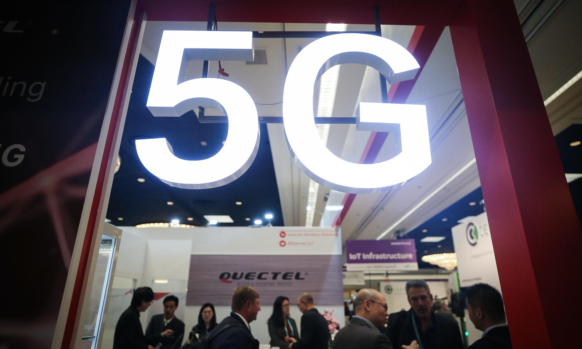Attendees and workers chat beneath a &#8216;5G&#8217; logo at the Quectel booth at CES 2020 at the Las Vegas Convention Center on January 8, 2020 in Las Vegas, Nevada. CES, the world&#8217;s largest annual consumer technology trade show, runs through January 10 and features about 4,500 exhibitors showing off their latest products and services to mo...