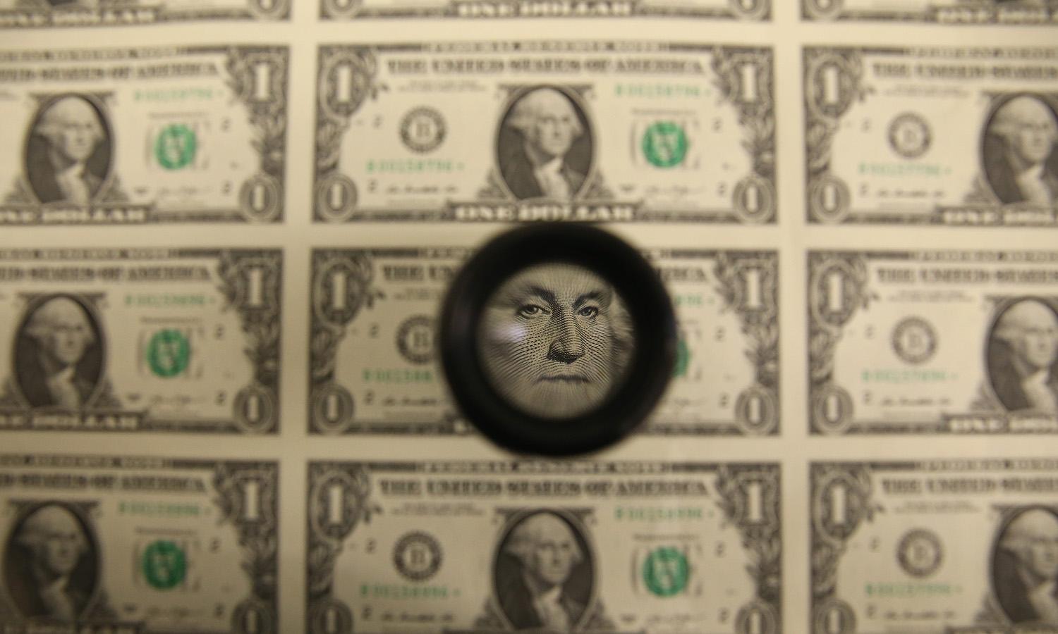 A magnifying glass is used to inspect newly printed $1 bills at the Bureau of Engraving and Printing on March 24, 2015, in Washington. (Photo by Mark Wilson/Getty Images)