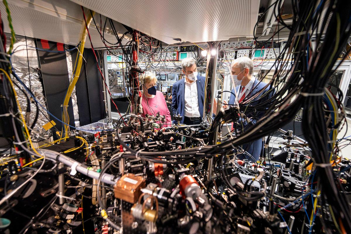 On Sept. 15,  2021, then-German Chancellor Angela Merkel, left, and Bavaria State Premier Markus Soeder, center, visit the Max Planck Institute of Quantum Optics in Garching, Germany, where institute manager Immanuel Bloch explains how a quantum computer works. (Photo by Guido Bergmann/Bundesregierung via Getty Images)
