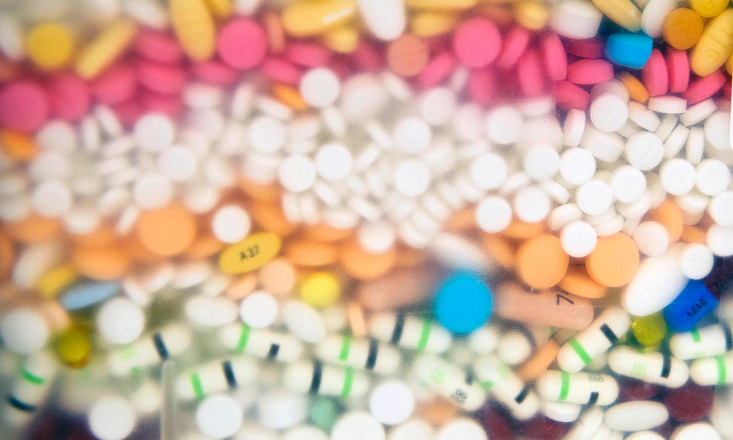 Multiple layers of pills of different colors sit in a pharmacy's pill disposal container.