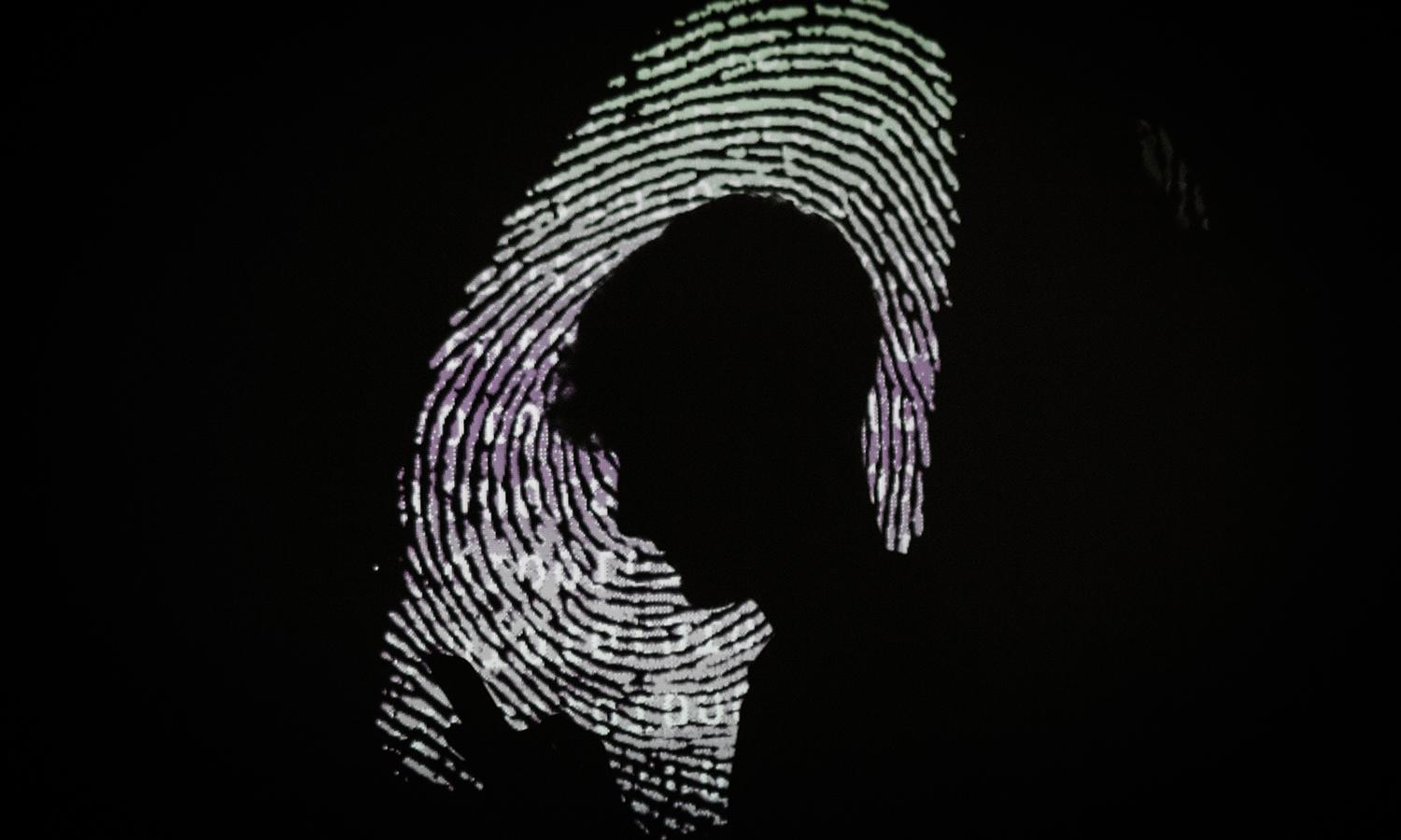 A man is seen using a mobile phone in the light of a projection of a thumbprint.