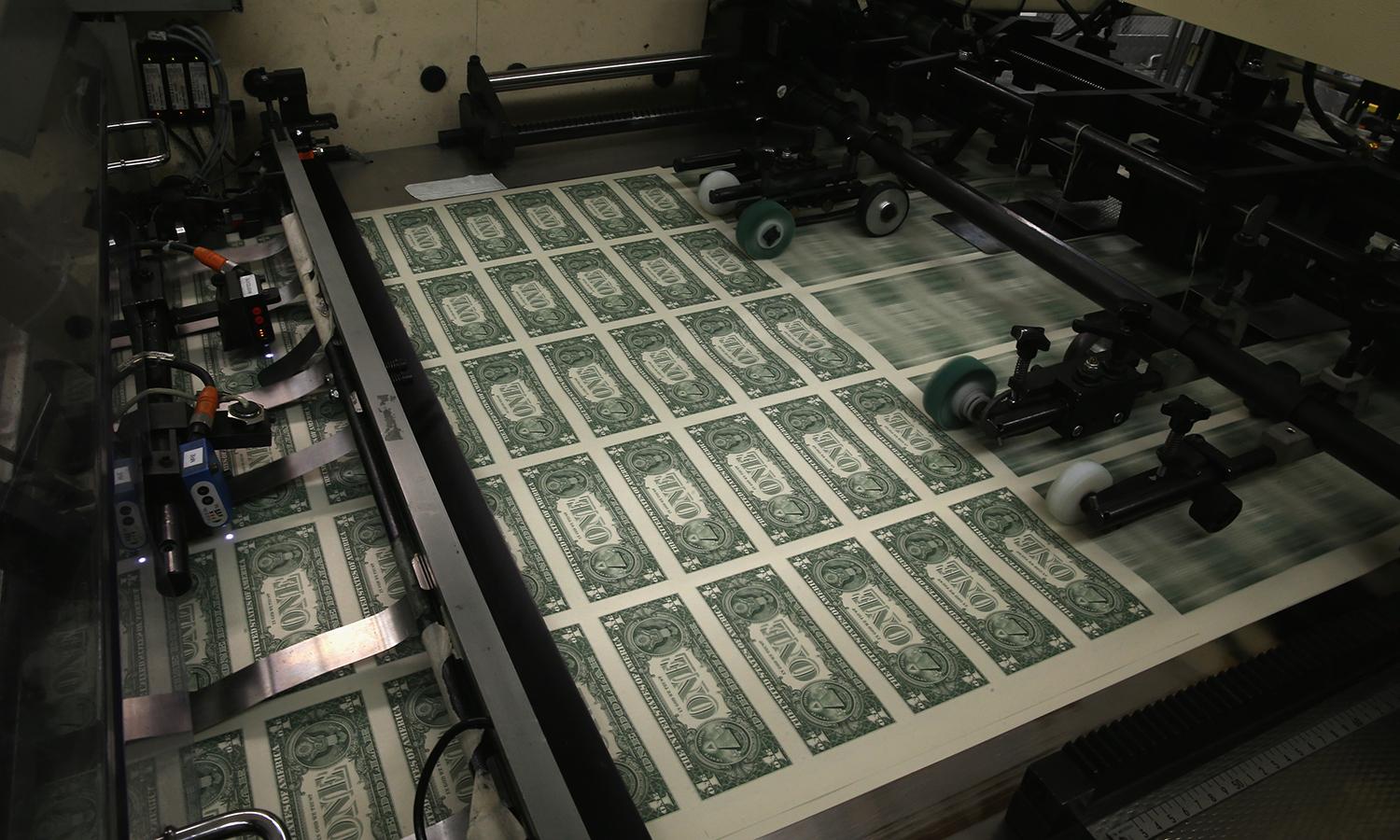 Sheets of one dollar bills run through the printing press.