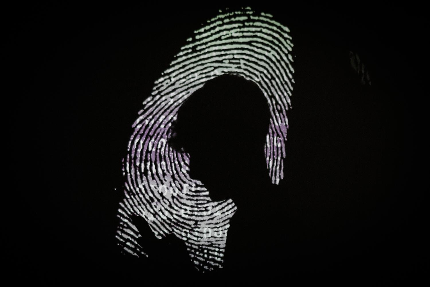 A man is seen using a mobile phone in the light of a projection of a thumbprint.